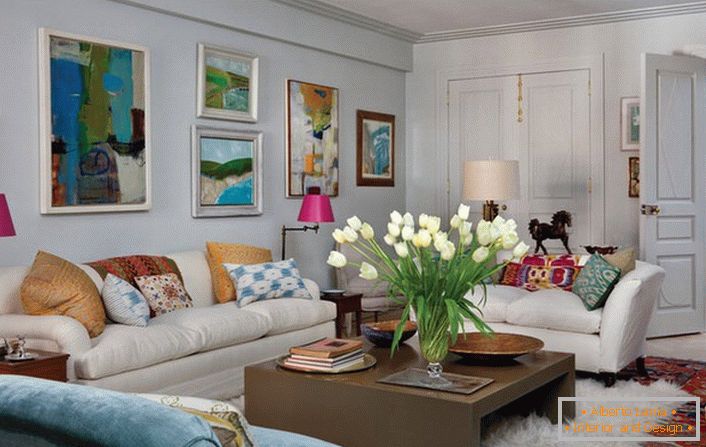 Univerzális nappali eklektikus stílusban. A hangulatos szoba sok párnát és absztrakt, fényes festményeket kínál, amelyek a kanapé feletti falat díszítik.
