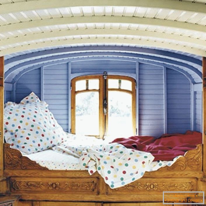 Minimális részletek a hálószobában a rusztikus stílusban. A tervező szokatlan helyet választott az ágyhoz. Az ablak melletti kis ágy tökéletes ágy az álmodók számára.