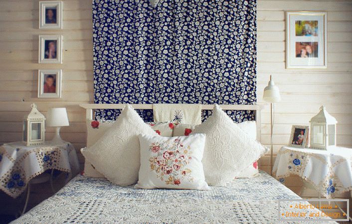 A rusztikus stílusnak megfelelően az ágyat pár párnák díszítik, kontrasztos vörös hímzéssel. Az éjjeliszekrényeket egy finom kék virágokkal díszített asztalterítő borítja.