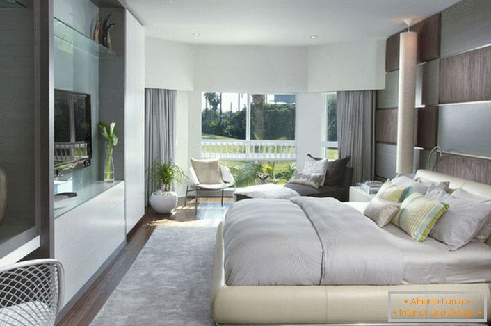 Puha, ömlesztett ágy a hálószobában modern stílusban. A fényes felületű bútorok jól illeszkednek a belső tér összetételéhez.